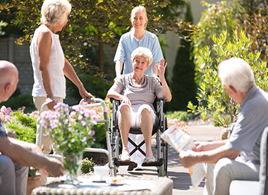 Caregiver Taking Senior Through Park with Other Seniors